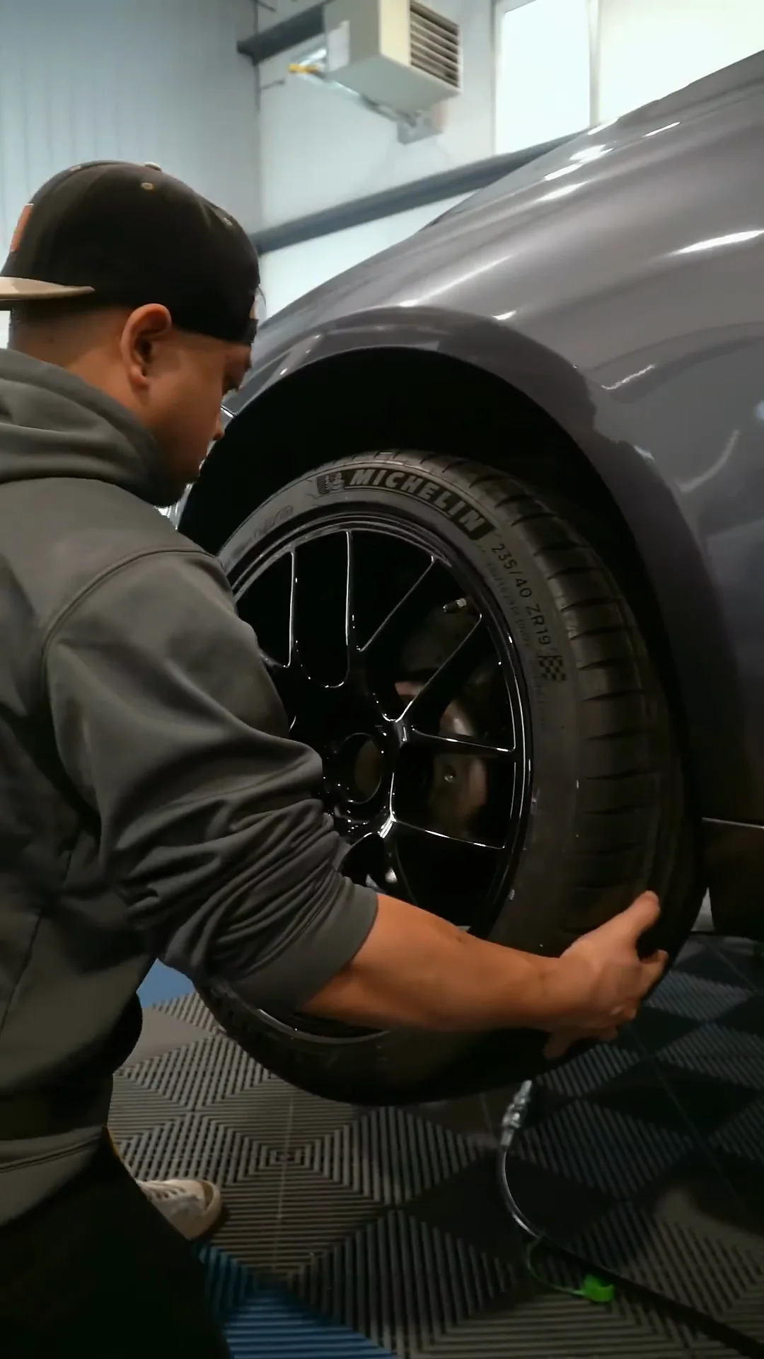 Technician fitting a black wheel to a gray BMW