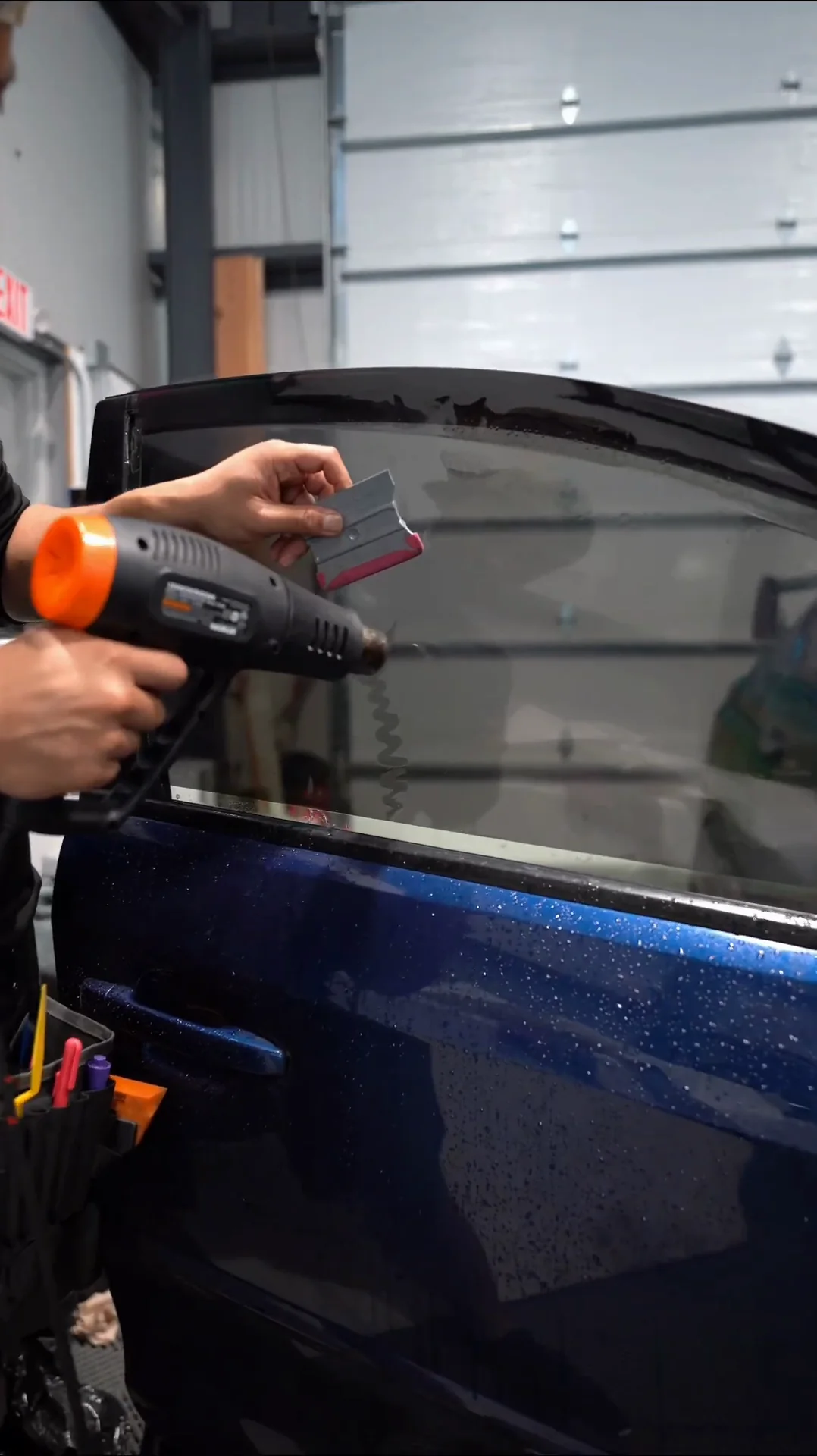Installer heat-shrinking window film on the door glass of a blue Subaru WRX