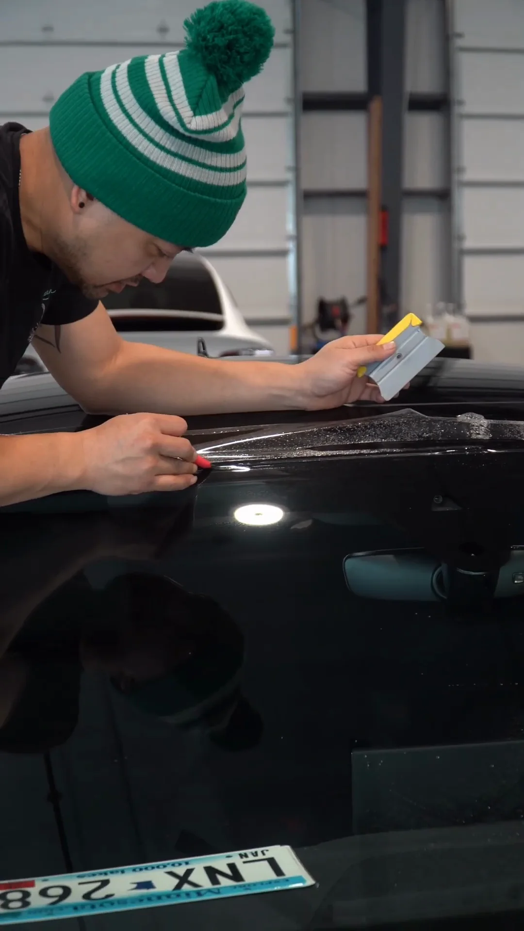 Installer in a green knit hat squeegeeing film on a windshield