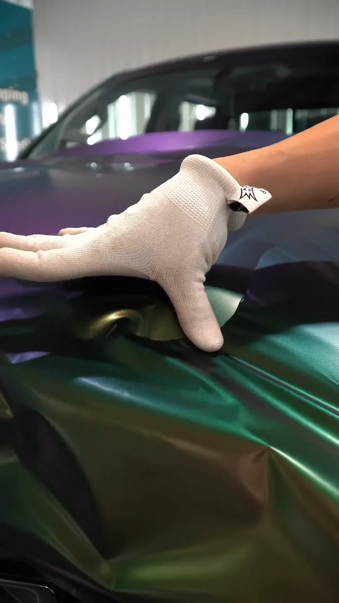 Gloved hand smoothing color-shift wrap film on a GMC hood